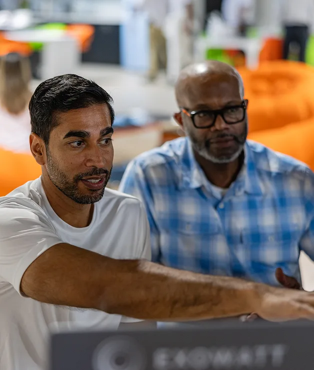 Two colleagues collaborating in an office, one pointing at a screen with focus while the other listens attentively, with Exowatt branding visible in the foreground.