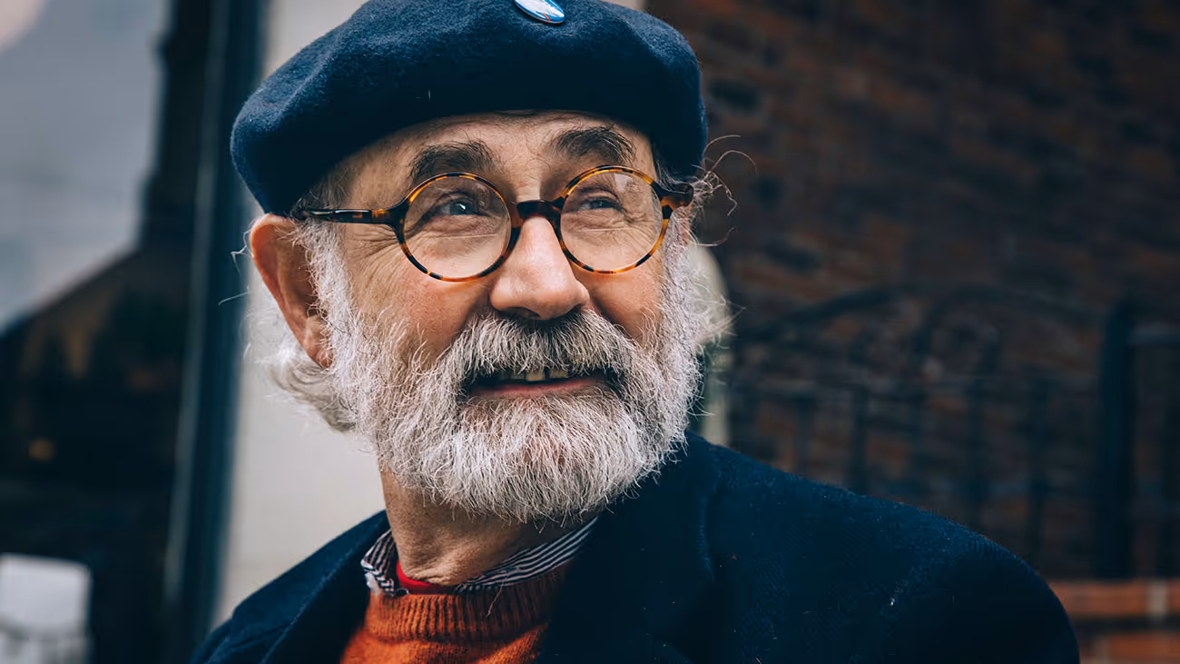 Elderly man with white beard, glasses, and beret smiling warmly
