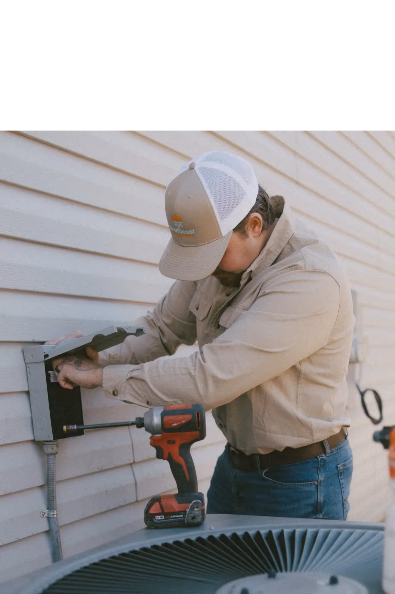 Technician working on electrical box with drill near air conditioning unit.