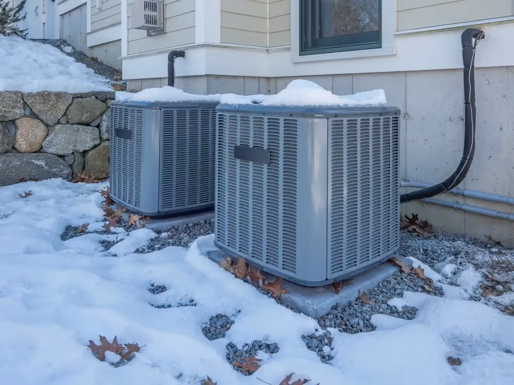 Snow-covered air conditioning units outside residential building in winter.
