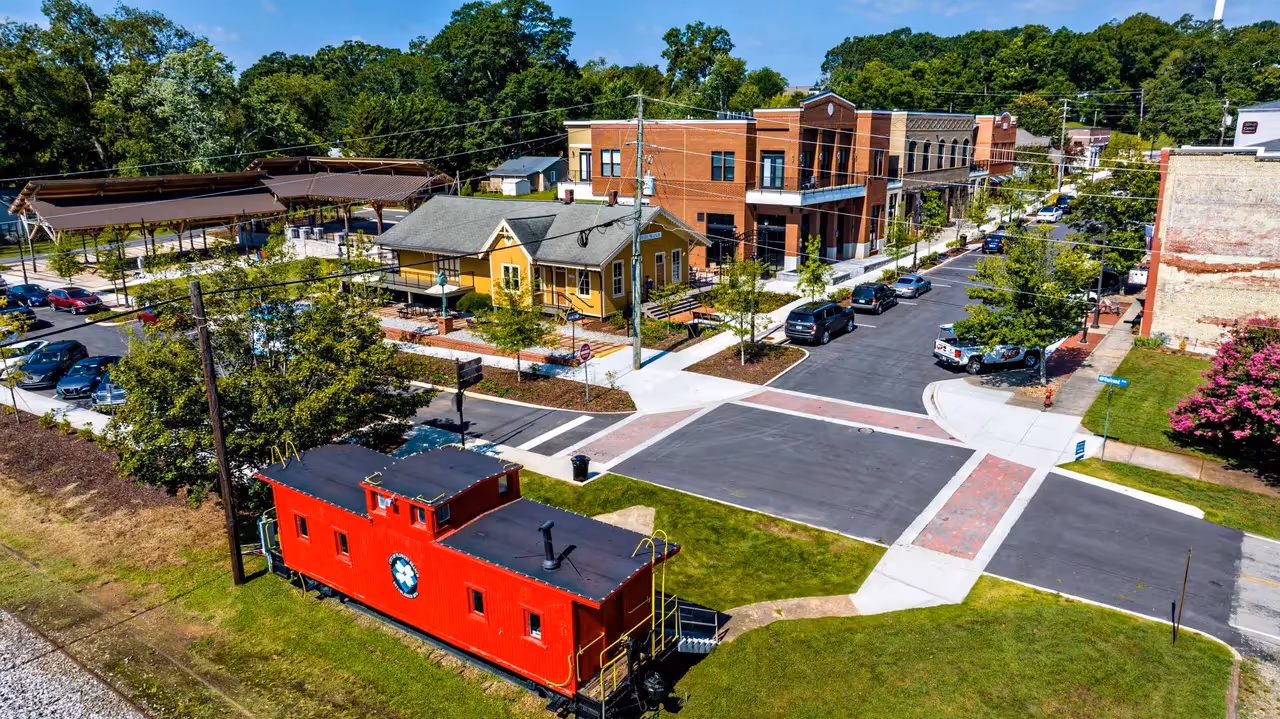 Bright red caboose parked in modern urban neighborhood with colorful buildings.