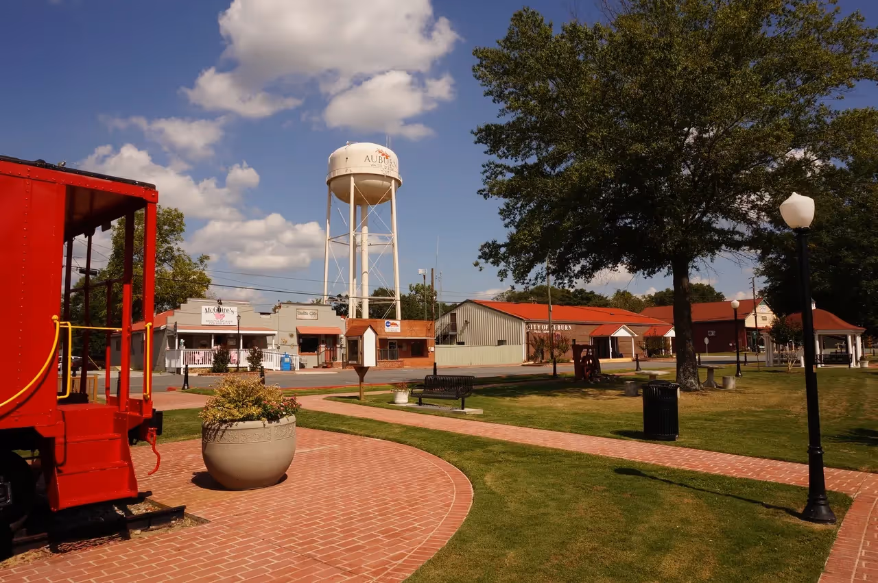 Auburn water tower and red caboose in small town park on sunny day.