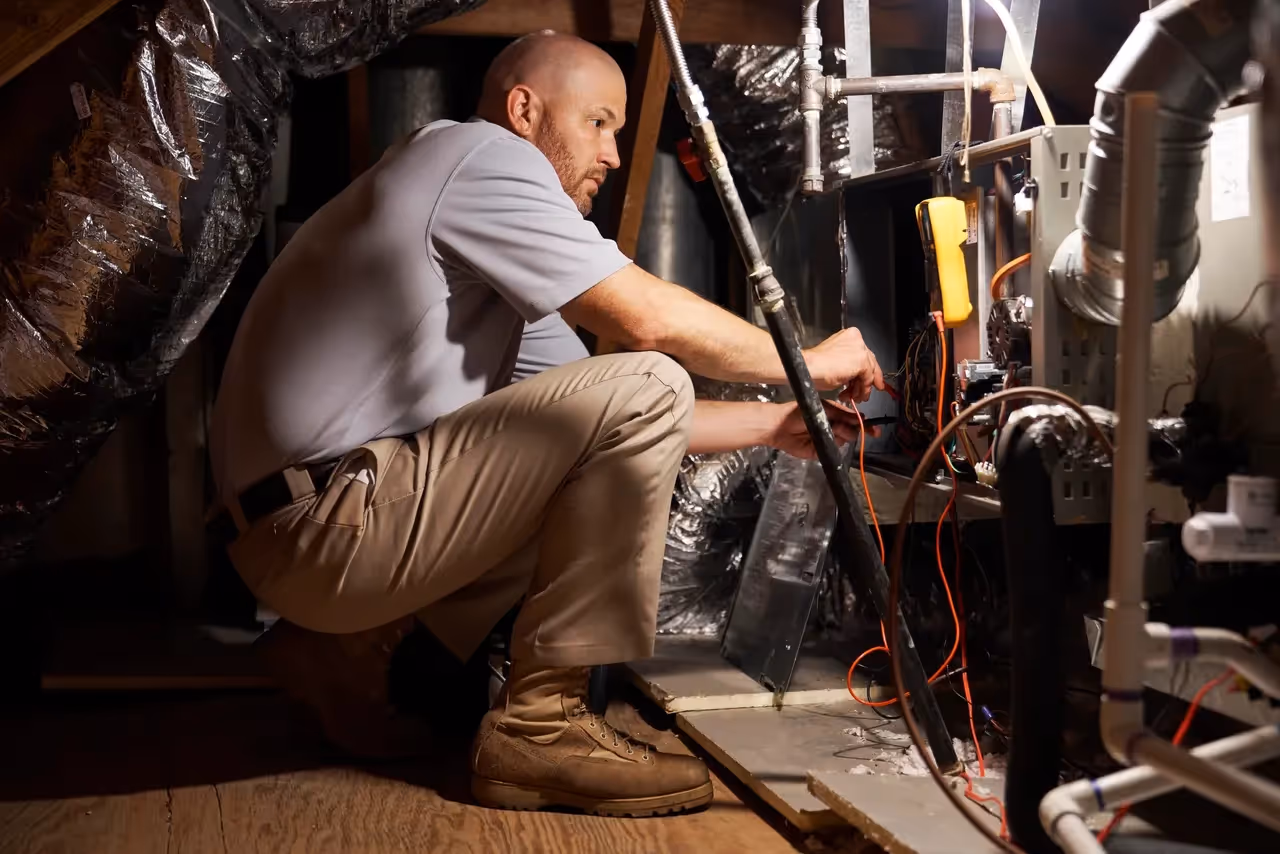 Technician crouching and inspecting electrical wiring in mechanical room.