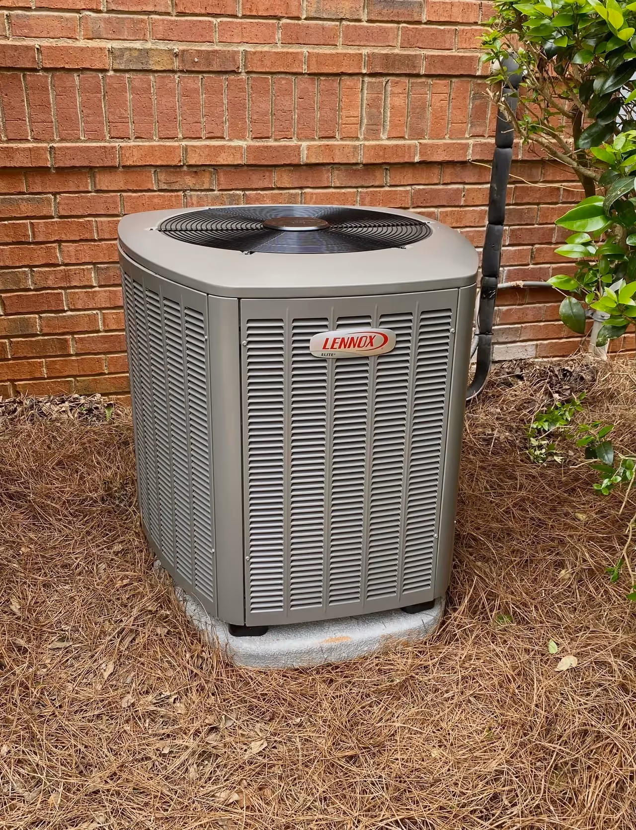 Lennox air conditioning unit installed on concrete pad near brick wall.