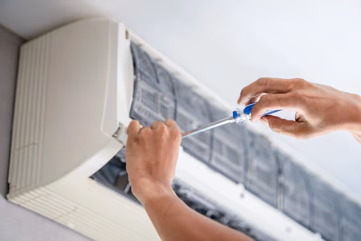 Person repairing air conditioning unit with screwdriver.