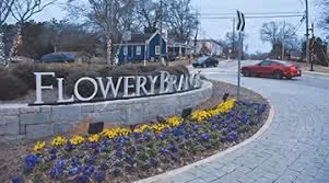 Flowery Lane entrance sign with colorful flower beds and red car nearby