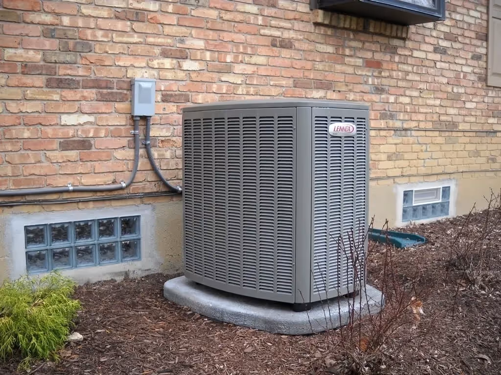 Lennox air conditioning unit installed on concrete pad next to brick house