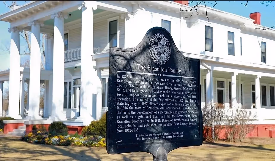 Historical marker describing the Braselton Family in front of white farmhouse