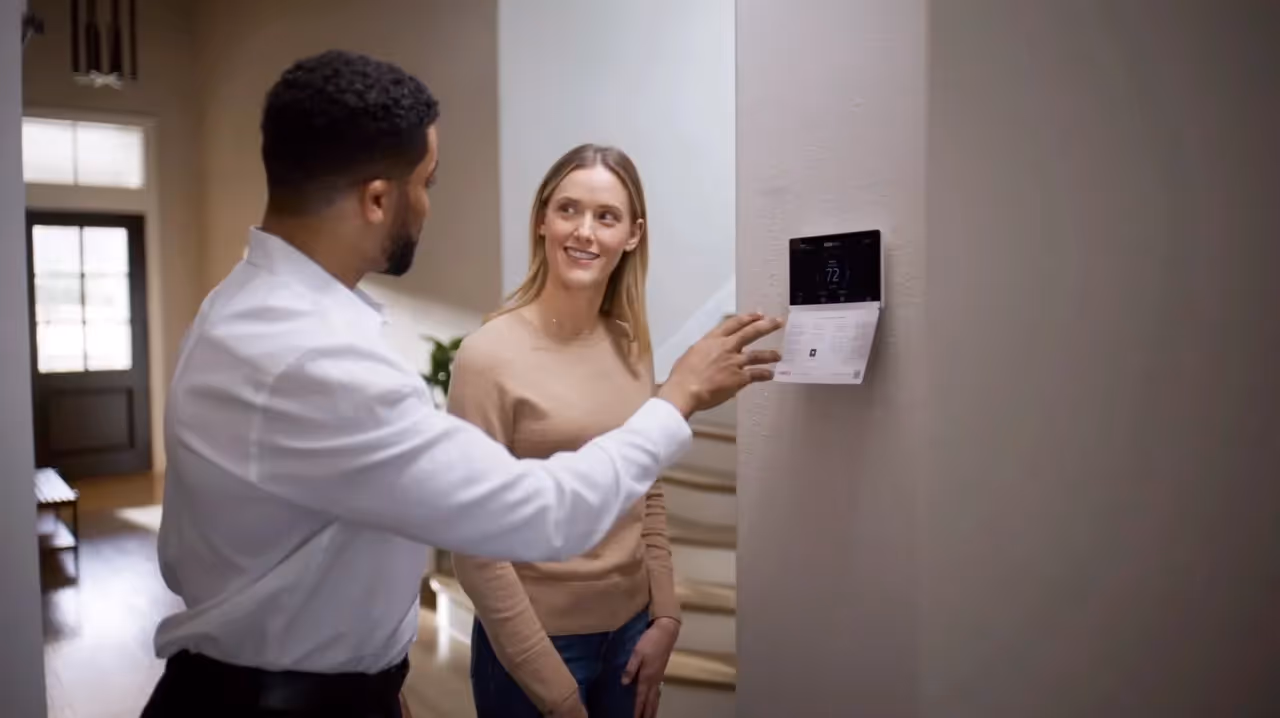Two people adjusting a smart thermostat in a home interior