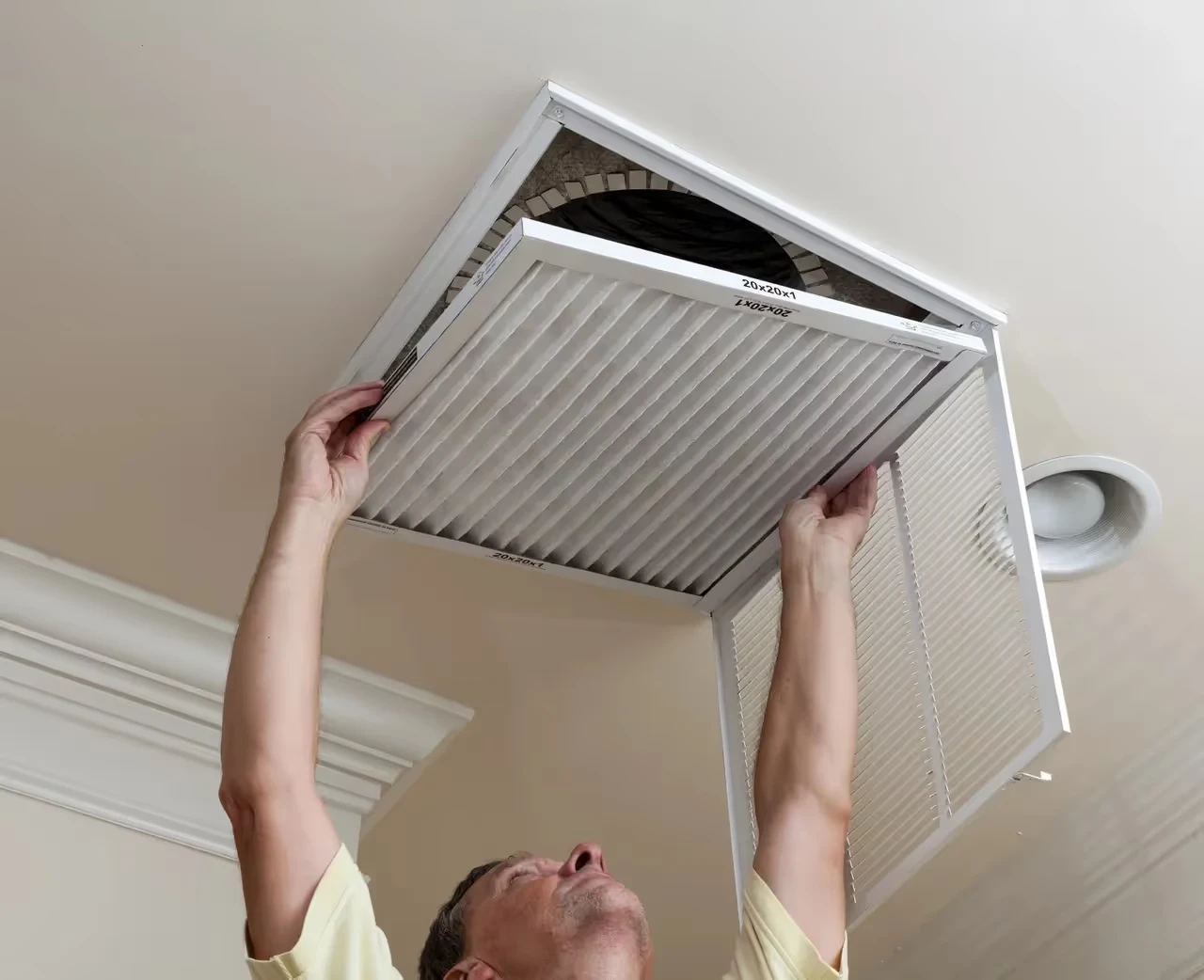 Person removing air filter from ceiling vent in home