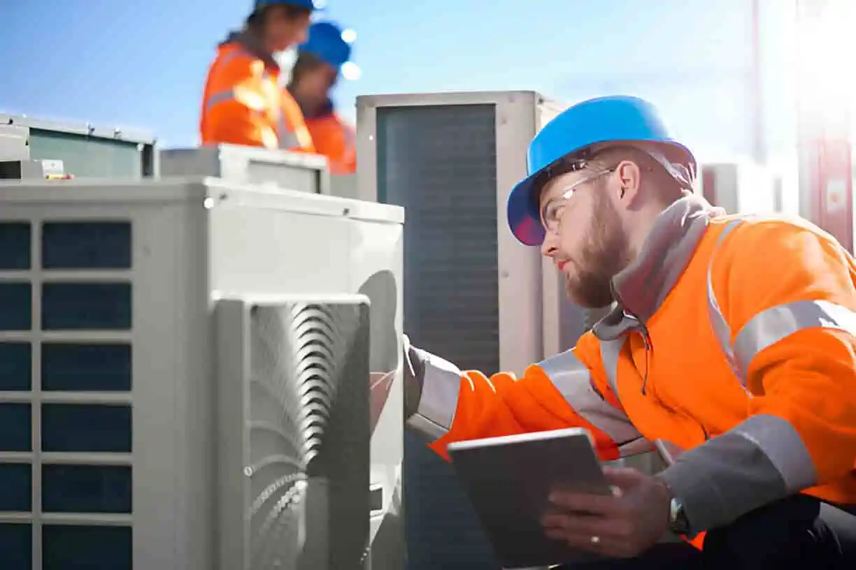 Technicians in safety vests inspect industrial equipment with tablet