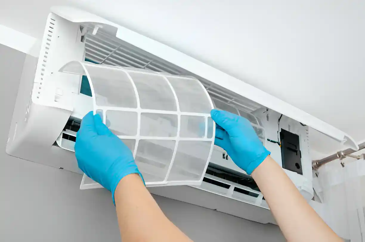 Hands in blue gloves removing air conditioner filter for cleaning