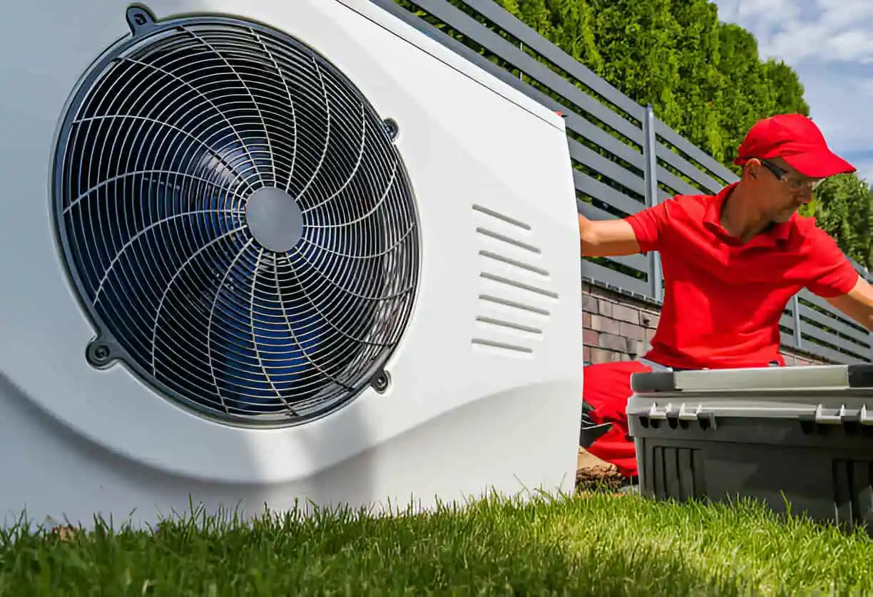 Air conditioning technician installing outdoor HVAC unit on grassy lawn
