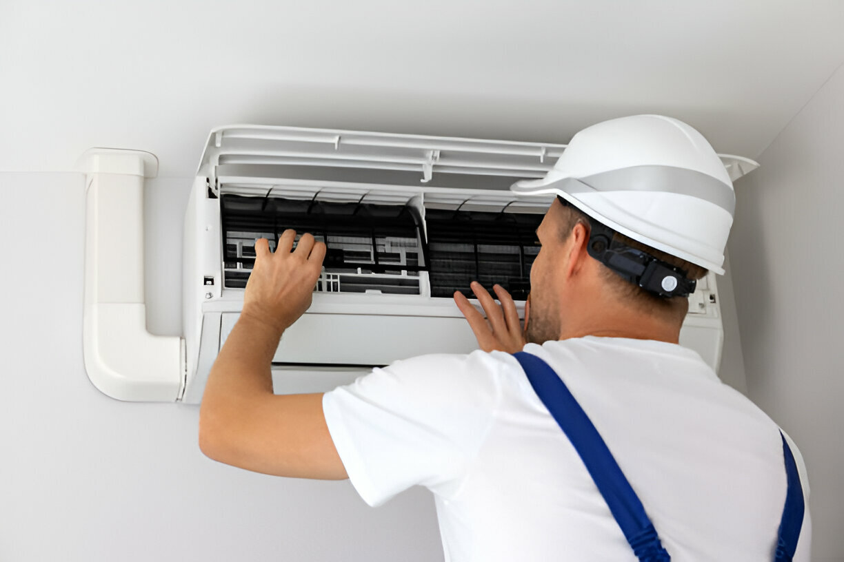 Technician in white helmet repairing air conditioning unit on wall