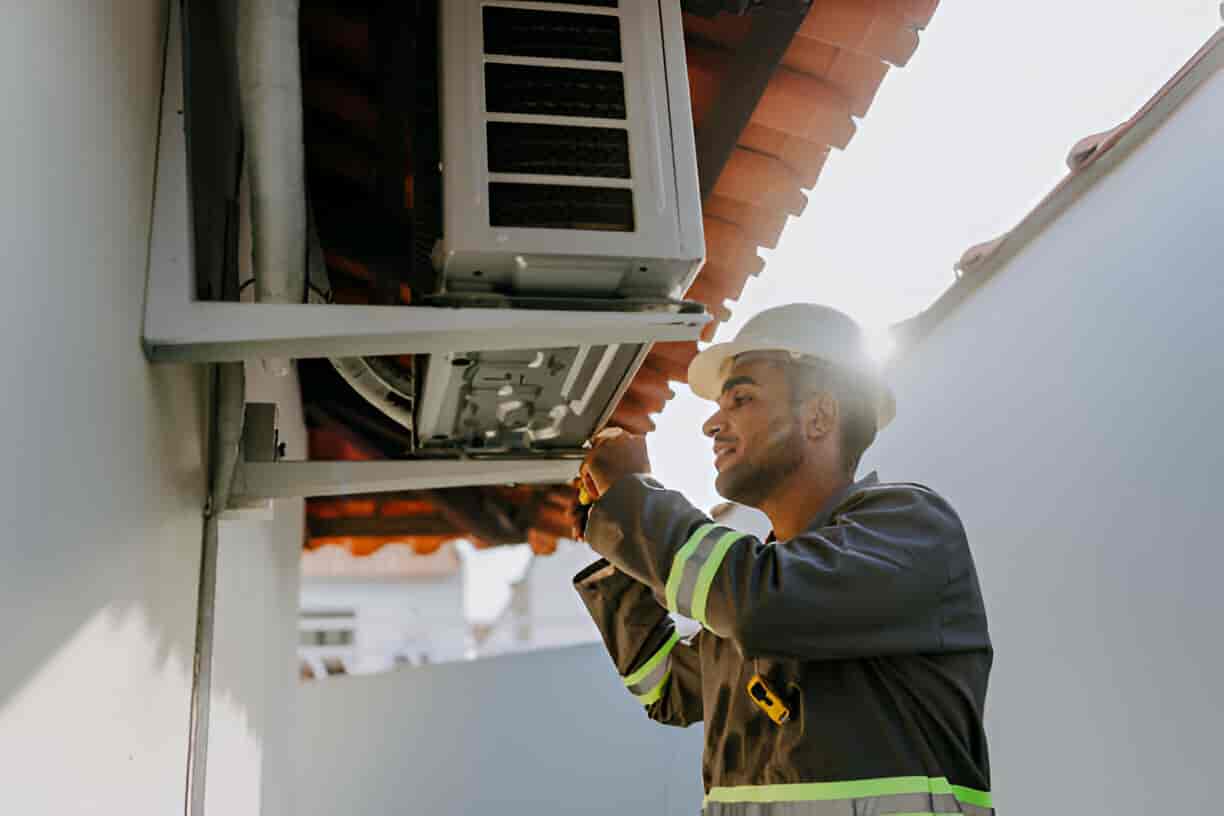 Technician in safety vest inspecting air conditioning unit on building exterior