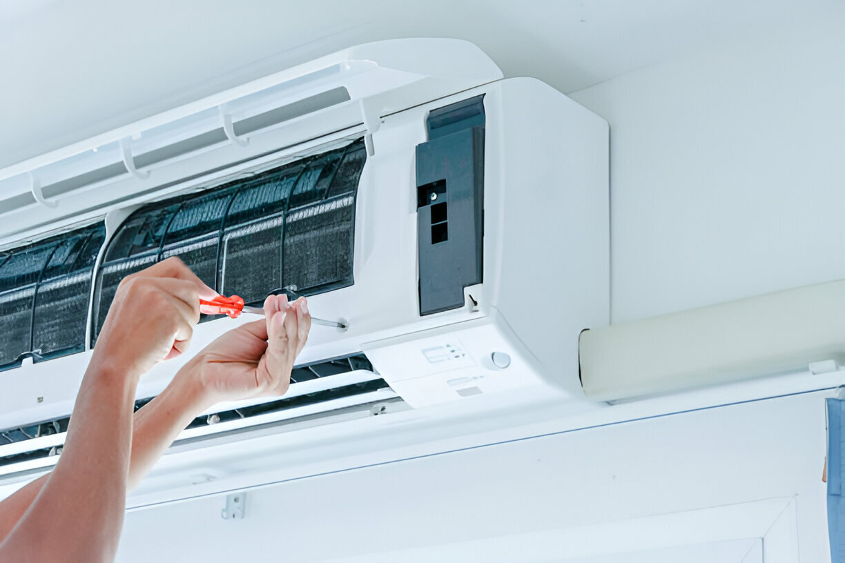 Hands repairing air conditioning unit with red screwdriver