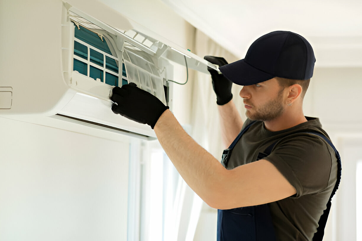 Technician in black gloves cleaning and maintaining a wall-mounted air conditioner