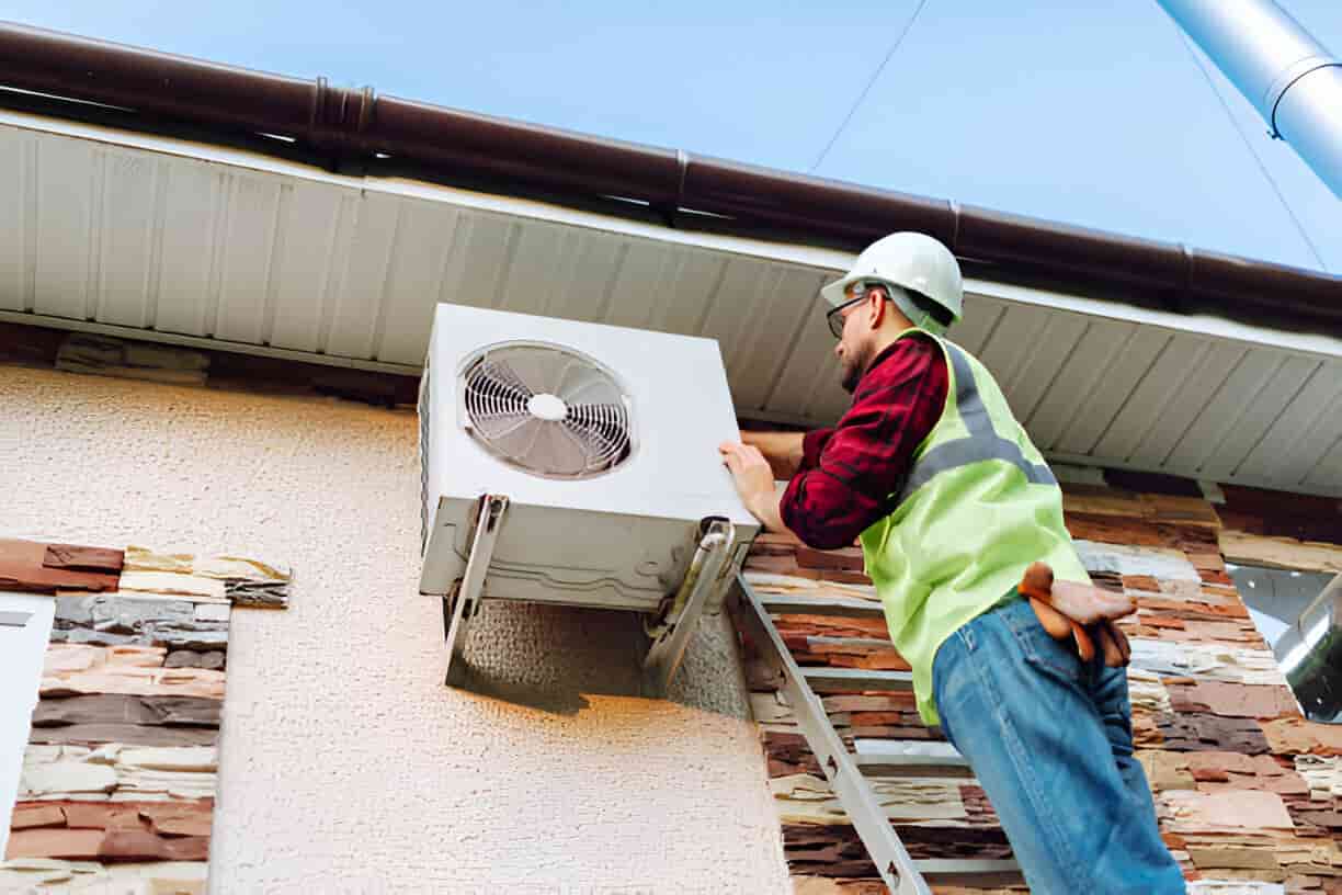 Technician in safety vest checking air conditioning unit on building exterior