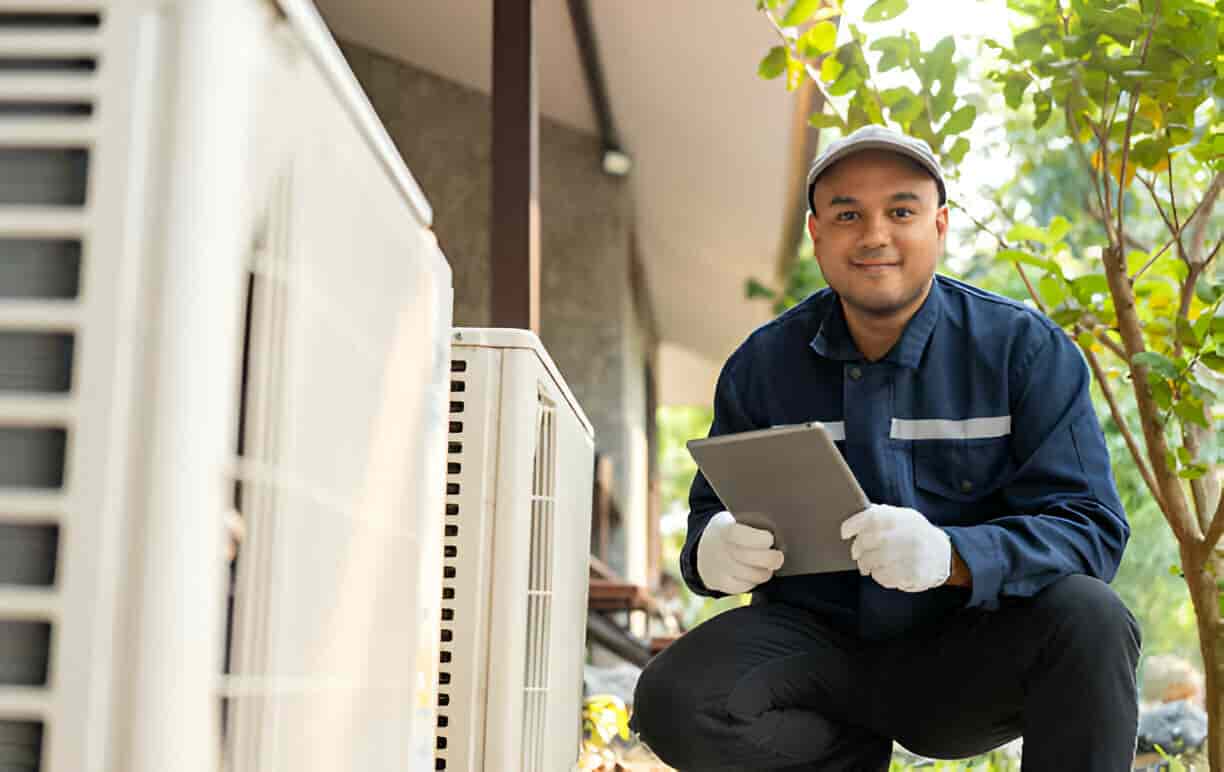 Technician in blue uniform checking air conditioning unit with tablet