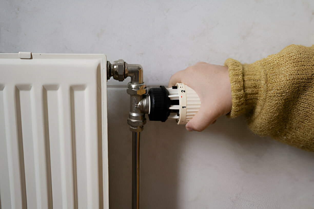 Hand adjusting thermostat on white radiator with metal valves