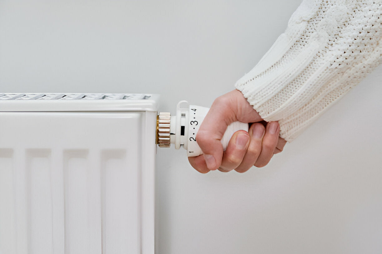 Hand adjusting white radiator thermostat in knitted sweater sleeve