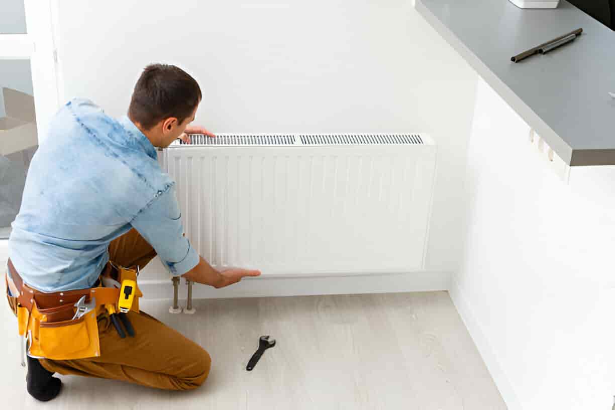 Technician installing or repairing a white radiator heating system