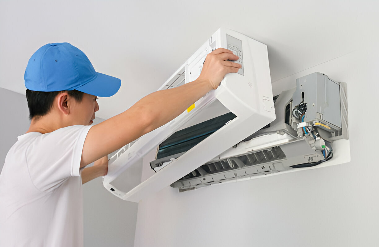 Technician in blue cap repairing wall-mounted air conditioning unit