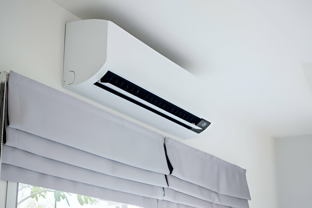 Wall-mounted air conditioner above a window with gray blinds