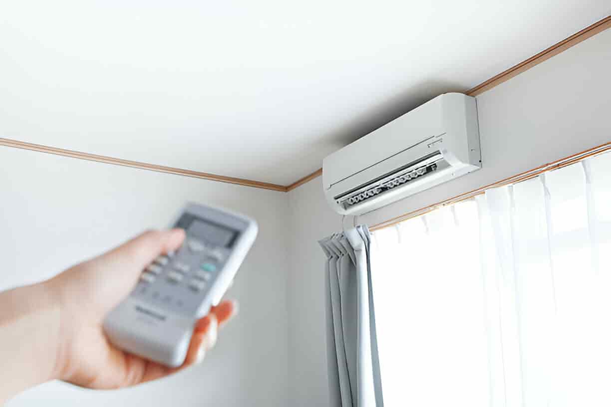 Hand holding remote control pointed at wall-mounted air conditioner