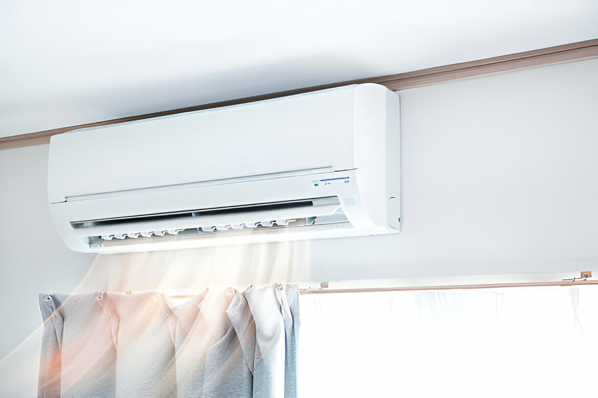 White air conditioning unit mounted on wall above soft pastel curtains