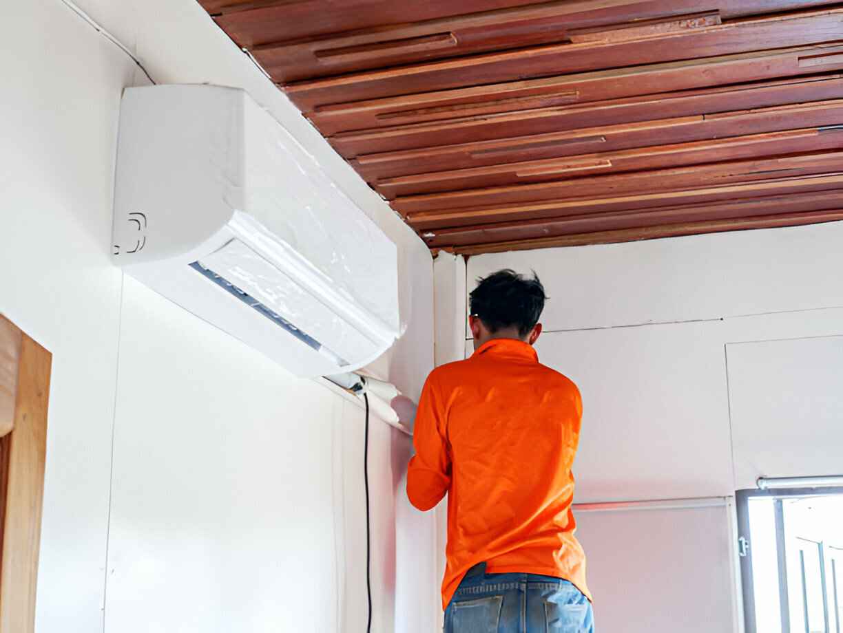 Technician in orange shirt installing or repairing wall-mounted air conditioner