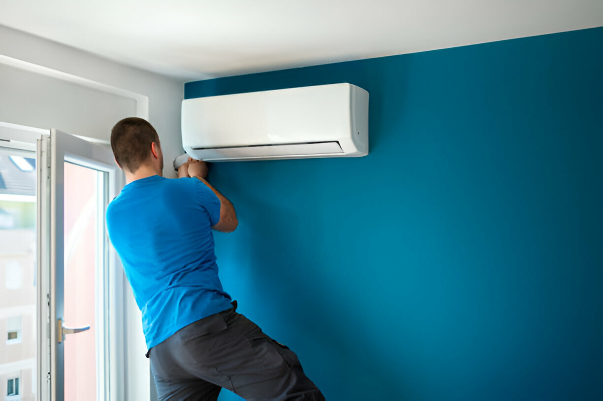 Person in blue shirt installing white air conditioning unit on teal wall