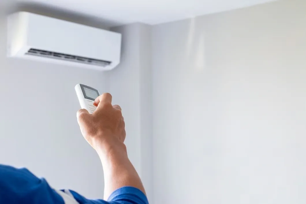 A hand holding an AC remote, pointing towards a wall-mounted AC unit.