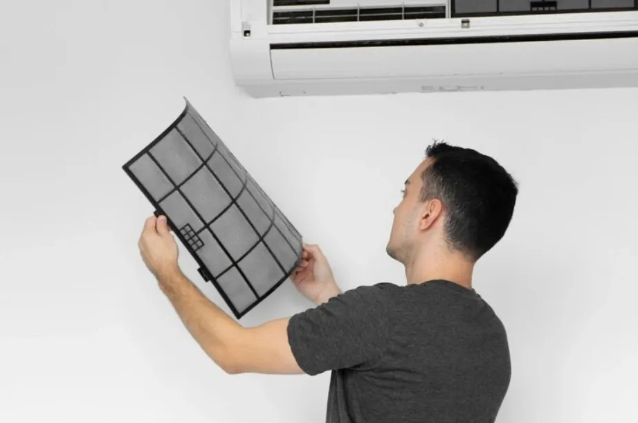 A man holding a clean air filter, inserting it into a wall-mounted AC unit.
