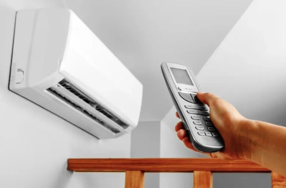 A hand holding an AC remote, pointed towards a wall-mounted AC unit.