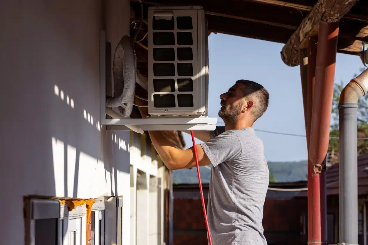 Technician installing outdoor air conditioning unit on building exterior