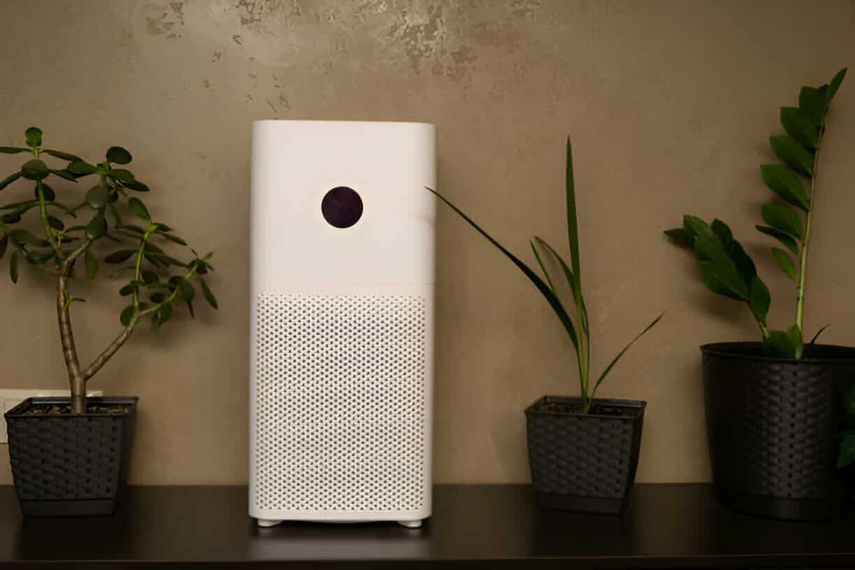 White air purifier with black circle on front, surrounded by potted plants