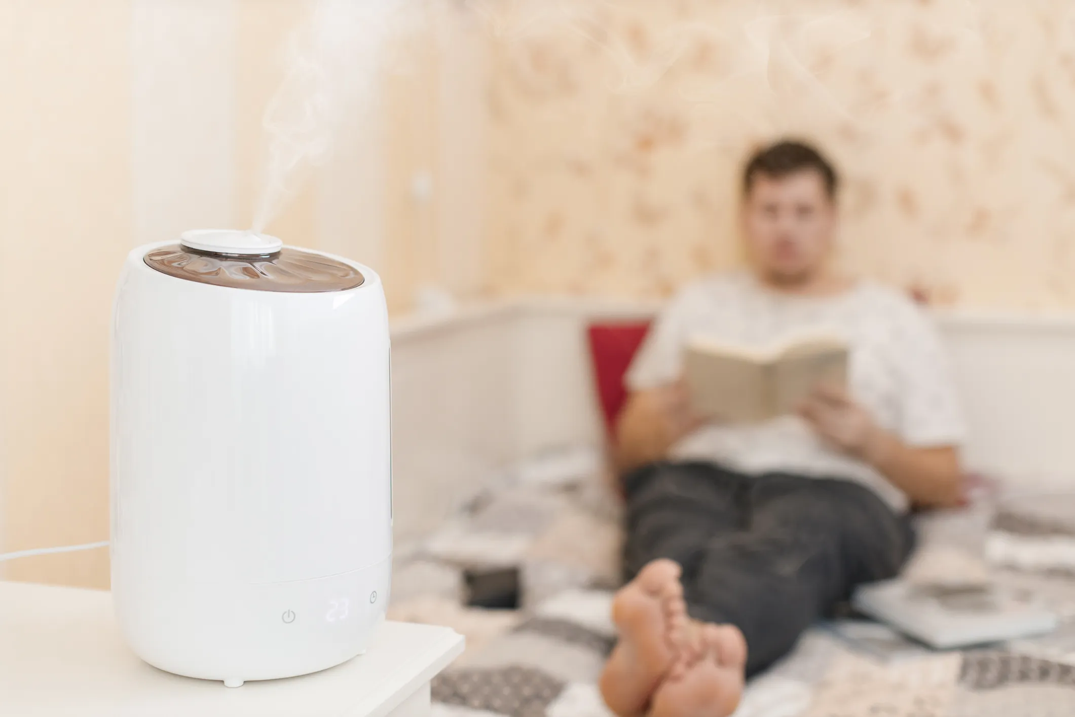 White air purifier near person reading book on bed at home