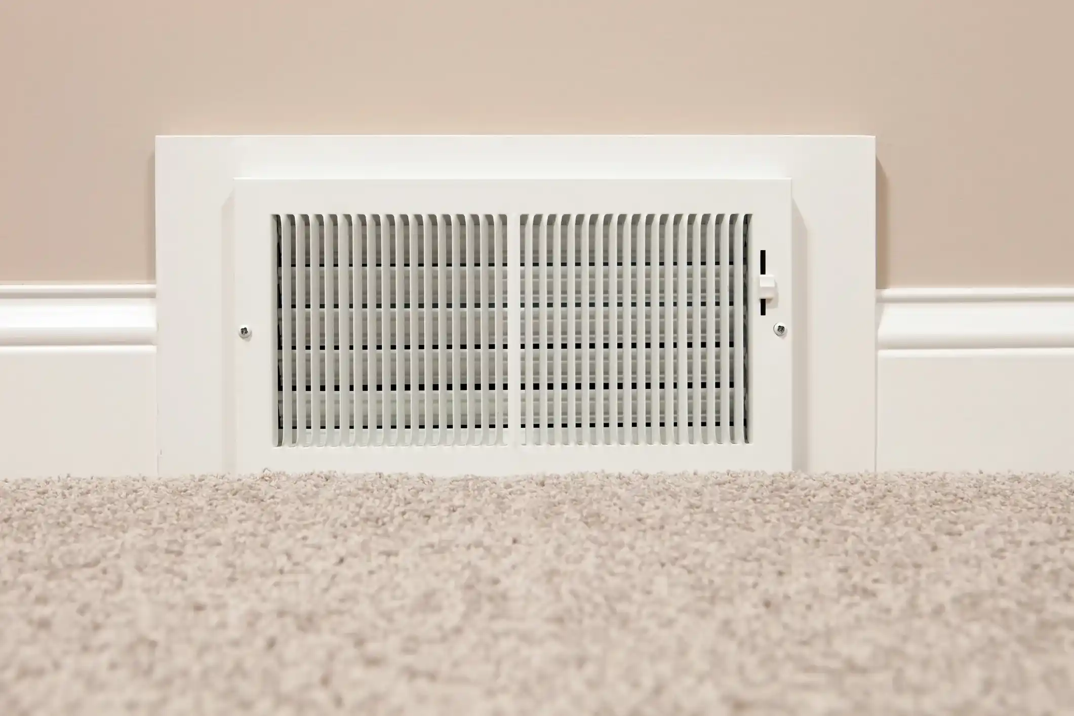 White air vent on beige wall above carpeted floor