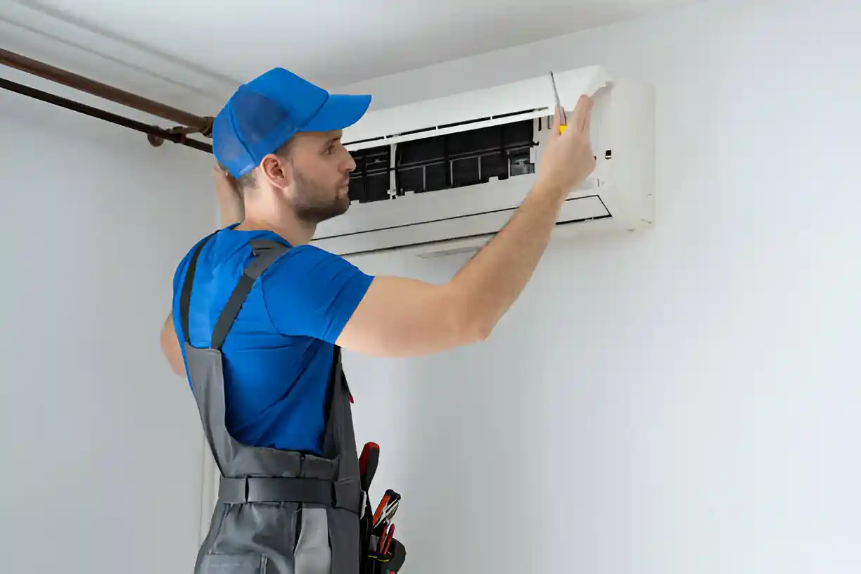 Technician in blue uniform repairing wall-mounted air conditioning unit