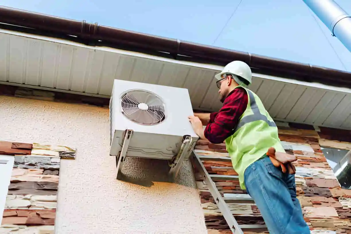 Technician in safety vest and hard hat repairs rooftop air conditioning unit
