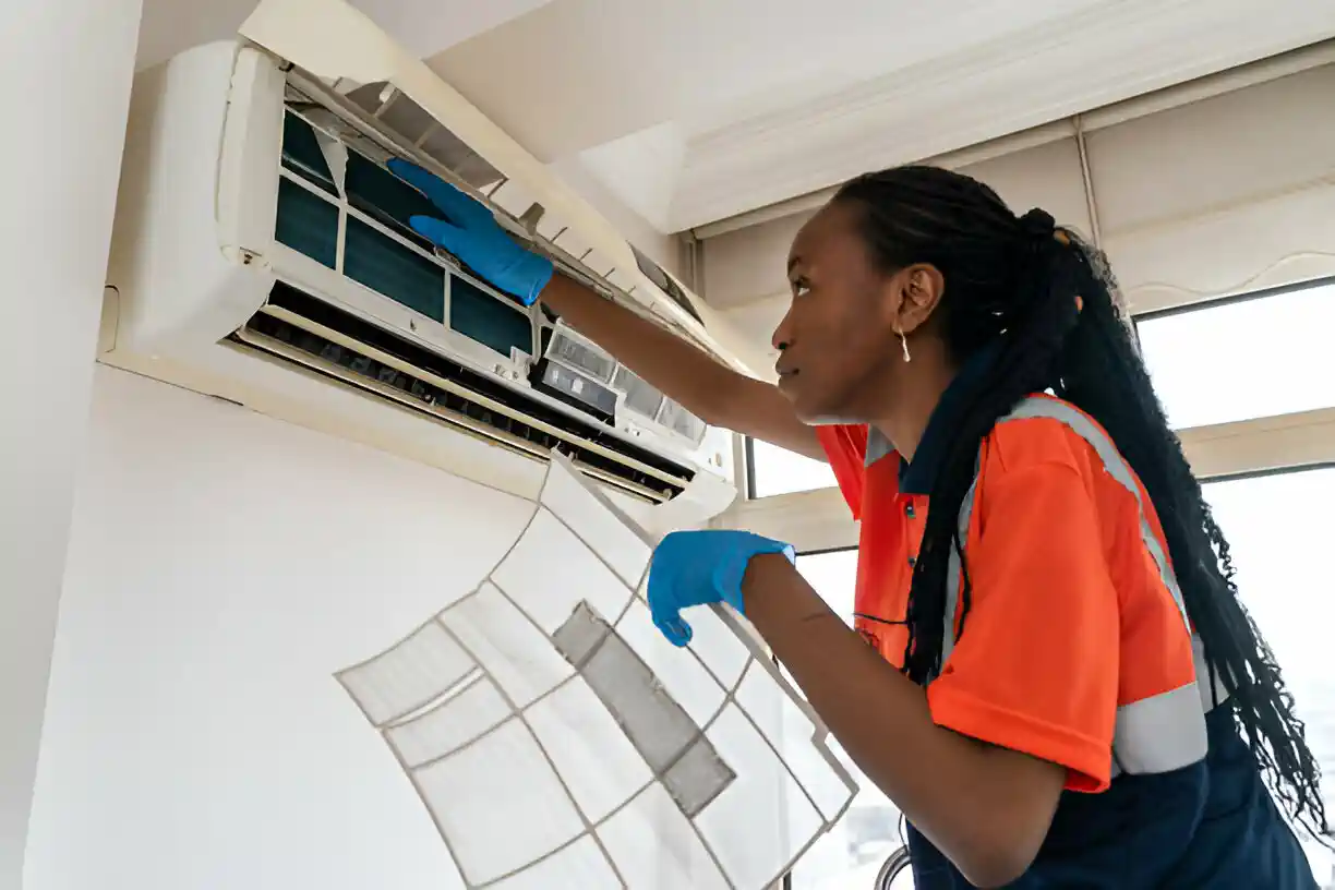 Technician in safety vest cleaning air conditioning unit with blue gloves