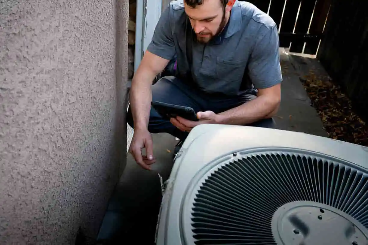 Technician checking HVAC unit with tablet near outdoor air conditioning system
