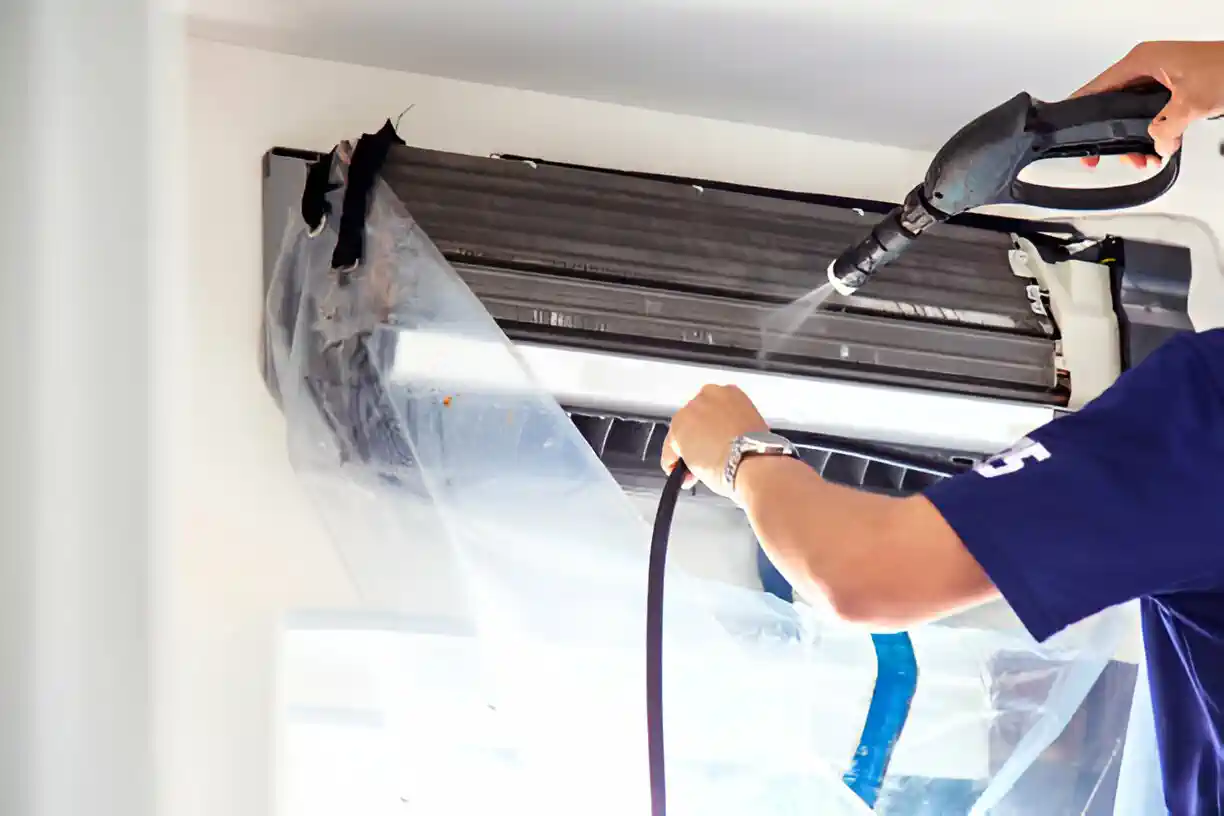 Technician cleaning air conditioning unit with high-pressure water spray
