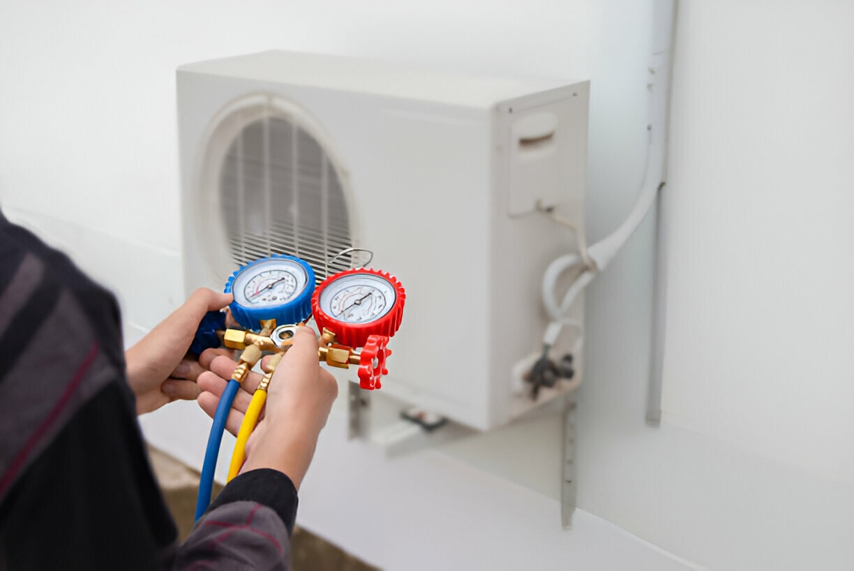 Technician checking air conditioning unit with colored pressure gauges