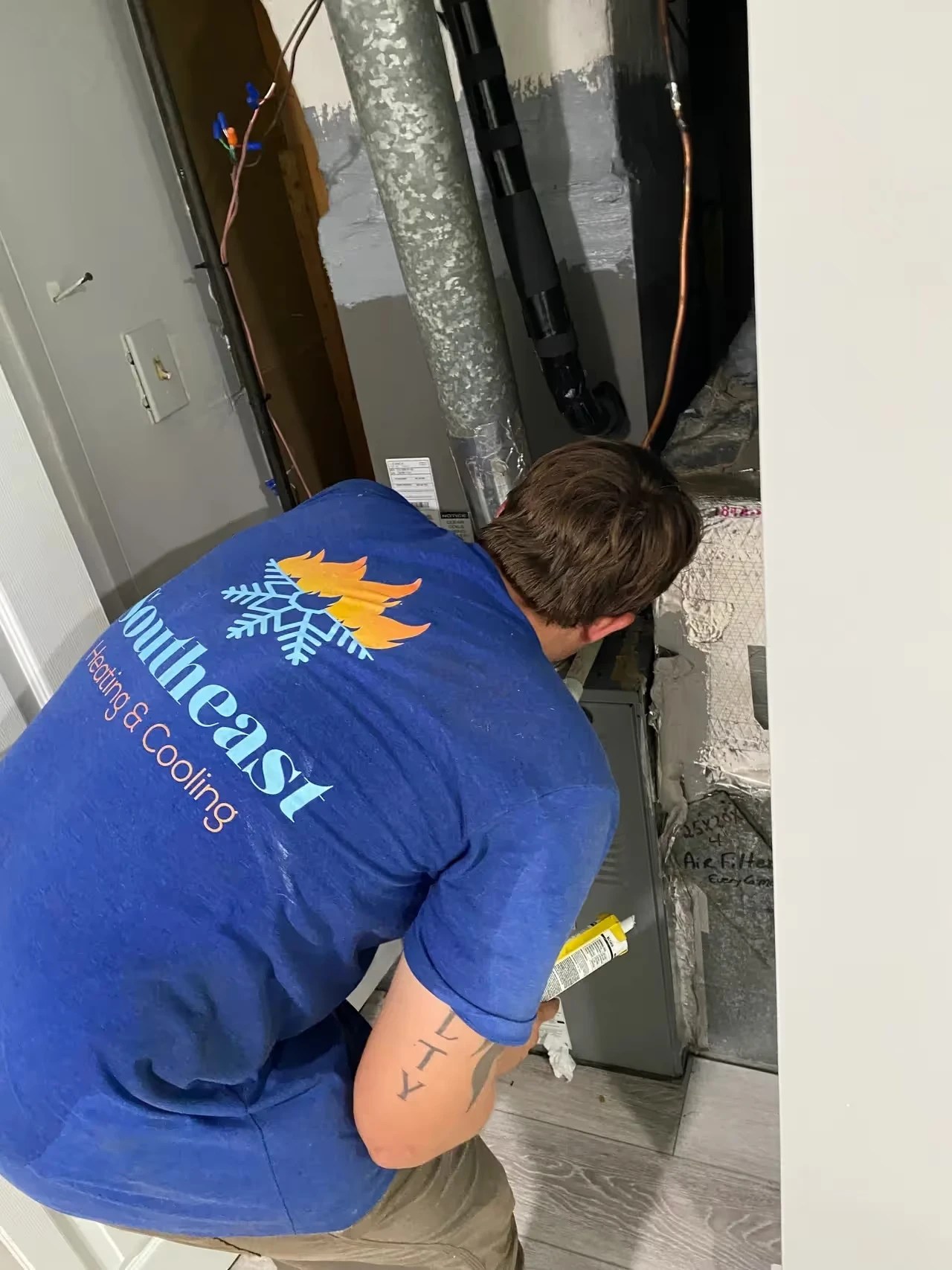 Technician in blue shirt repairing HVAC system near metal ductwork