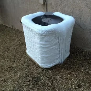 Frosted air conditioning unit covered in ice on grassy ground