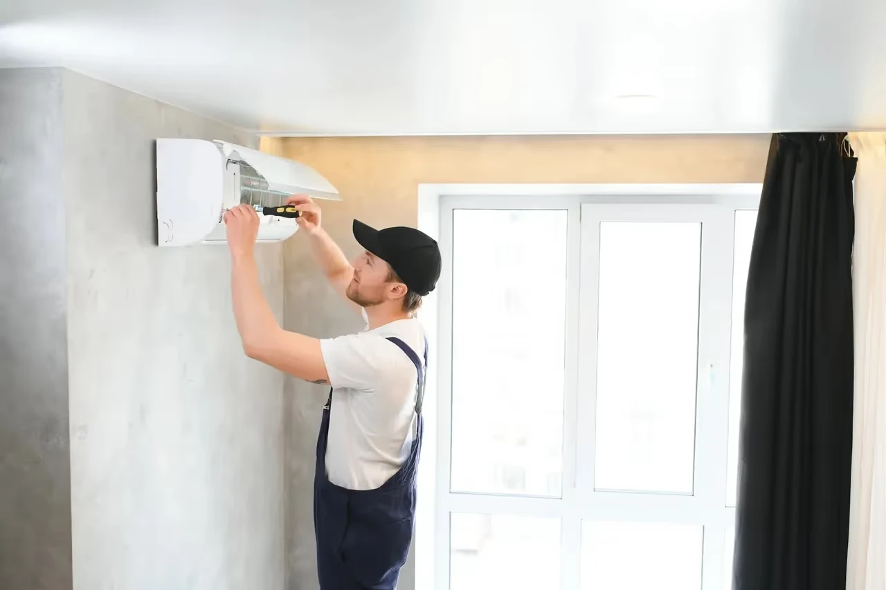Worker installing air conditioning unit on white wall near window