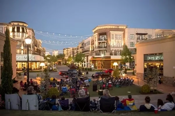 Outdoor community gathering at twilight in urban shopping district with string lights