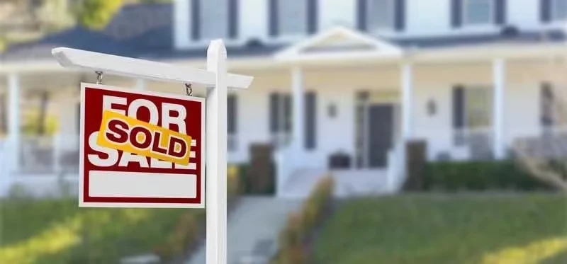 Sold real estate sign in front of white suburban house